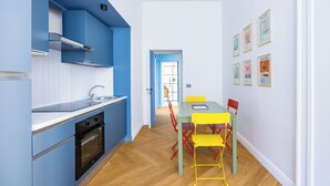 Une cuisine moderne avec des meubles bleus, un plancher en bois et un coin repas avec des chaises jaunes et une table verte.