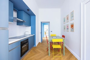 A modern kitchen with blue cabinets, a wooden floor, and a dining area with yellow chairs and a green table.
