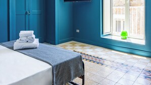 Une chambre d’hôtel avec un lit, un téléviseur fixé au mur, une fenêtre donnant sur l’extérieur et une porte bleue.