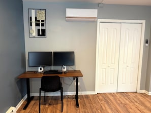 A room with a desk, two monitors, a chair, an air conditioning unit, and a white door. - Chicago 1BR Near Lake Michigan & Pratt Beach – Free Parking (Chicago)