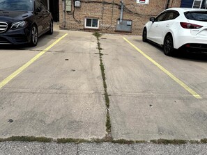 A parking lot with two cars parked, a visible crack in the pavement, and a building with brick walls in the background. - Chicago 1BR Near Lake Michigan & Pratt Beach – Free Parking (Chicago)