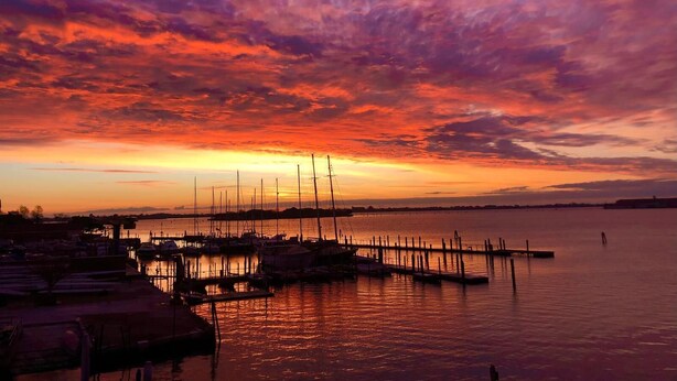 Satamassa auringonlaskun aikaan, jossa veneet ovat laiturissa ja tyyni vesi heijastaa taivasta.