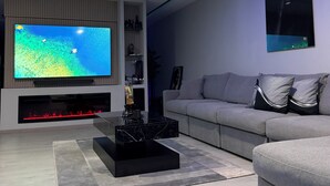 A modern living room with a flat-screen TV, a black coffee table, a grey sofa, and blue LED strip lighting.