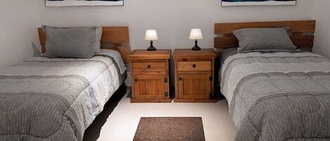 Une chambre avec deux lits jumeaux, deux tables de chevet, un tapis et des œuvres d’art accrochées au mur.