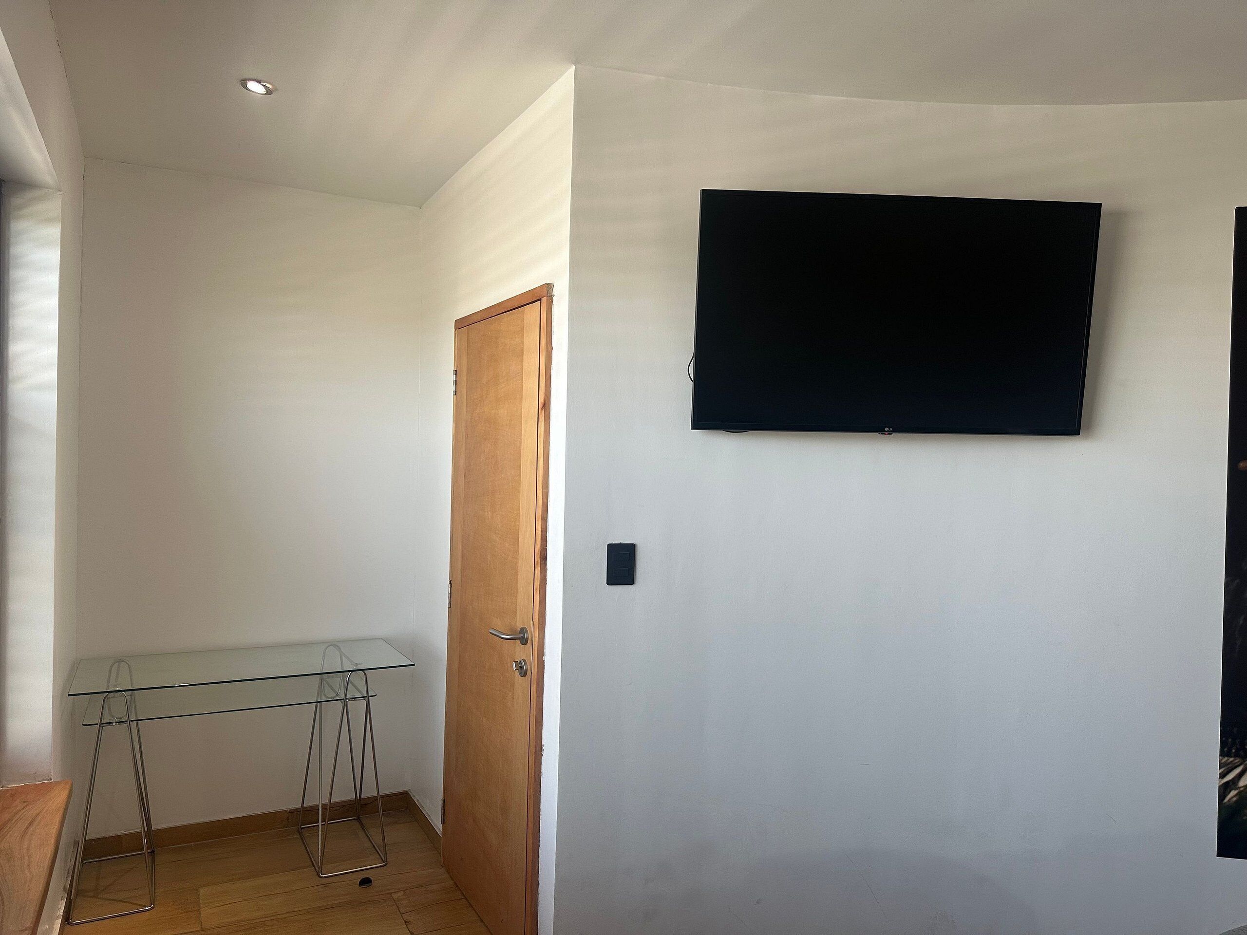 A room with a wooden door, a glass table, and a mounted flat-screen TV.