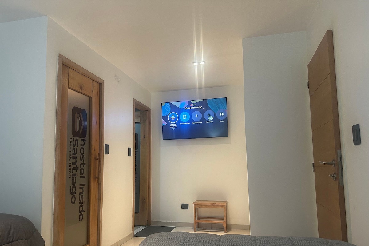 A hotel room with a bed, a television mounted on the wall, and a door labeled "hostel inside".