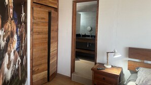 A bedroom with a wooden wardrobe, a mirror, a bedside table with a lamp, and a bed. - Hotel Inside (Santiago)