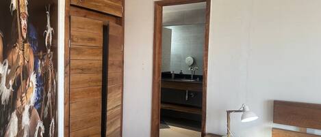 Un dormitorio con un armario de madera, un espejo, una mesita de noche con lámpara y una cama.