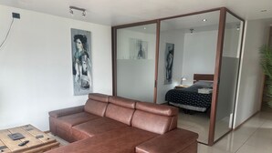 Un salon moderne avec un canapé en cuir marron, une table basse en bois et un lit recouvert d’une couvre-lit à motifs.