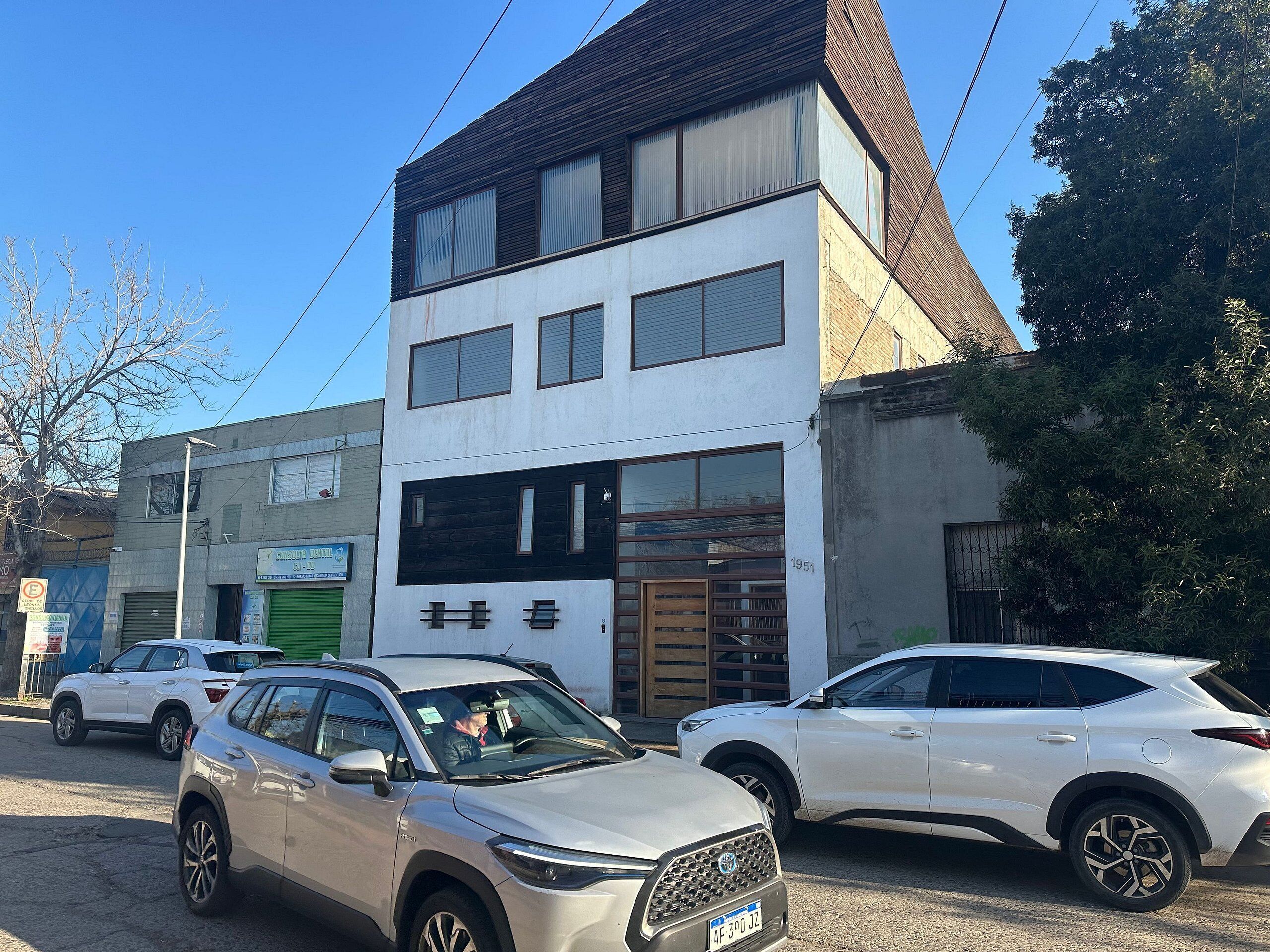 Un edificio moderno de dos pisos, con escaparate visible y coches aparcados en la parte delantera.