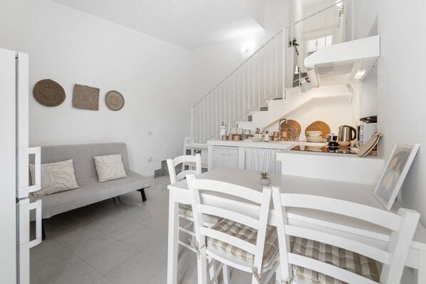A modern kitchen with white cabinetry, a dining table with chairs, a staircase, and a grey sofa.
