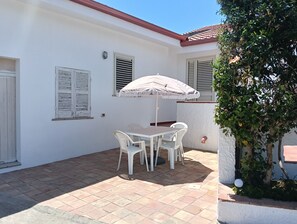 A patio with a table and chairs, a white wall, and a tiled floor.