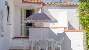 A patio with a table and chairs, a white umbrella, and a white wall with a door. - Holiday Home 'Istella - A' with Private Terrace (Sant'Anna Arresi)