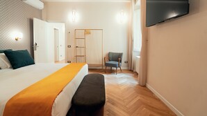 A hotel room with a bed, a bench, a chair, a TV, and a wardrobe. - Casa Mia Navona (Rome)