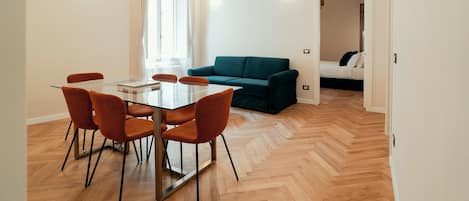 Una sala de estar moderna con una mesa de comedor de vidrio, sillas naranjas y un sofá color turquesa.