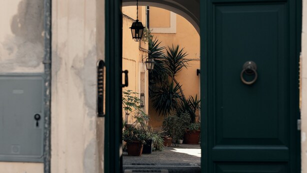 A green door with a metal handle, leading to a courtyard with potted plants and a lamp post. - Casa Mia Navona (Rome)