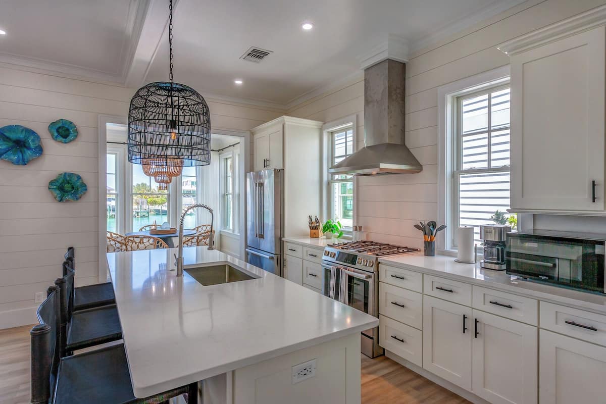 A modern kitchen with white cabinetry, a central island, stainless steel appliances, and decorative glass art.