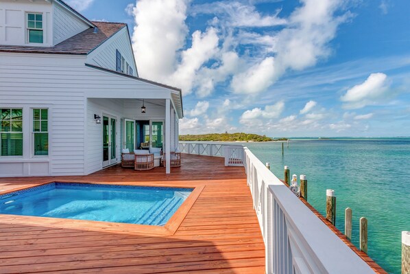 A white house with a wooden deck, a swimming pool, and a view of the ocean.