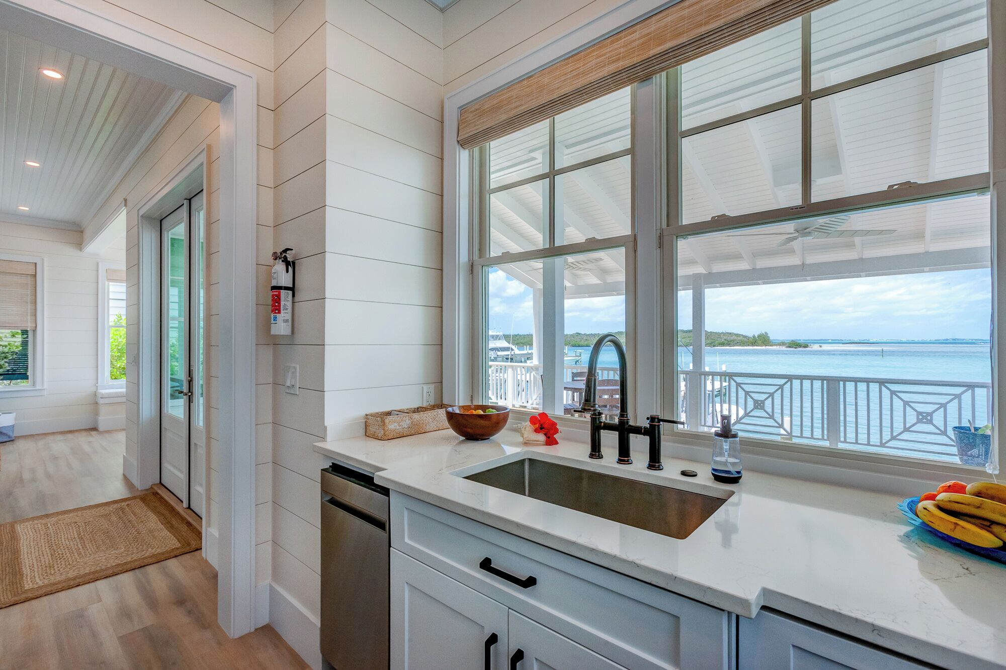 Una cocina moderna con un amplio ventanal con vista a un puerto deportivo, muebles de cocina blancos y un lavaplatos de acero inoxidable.
