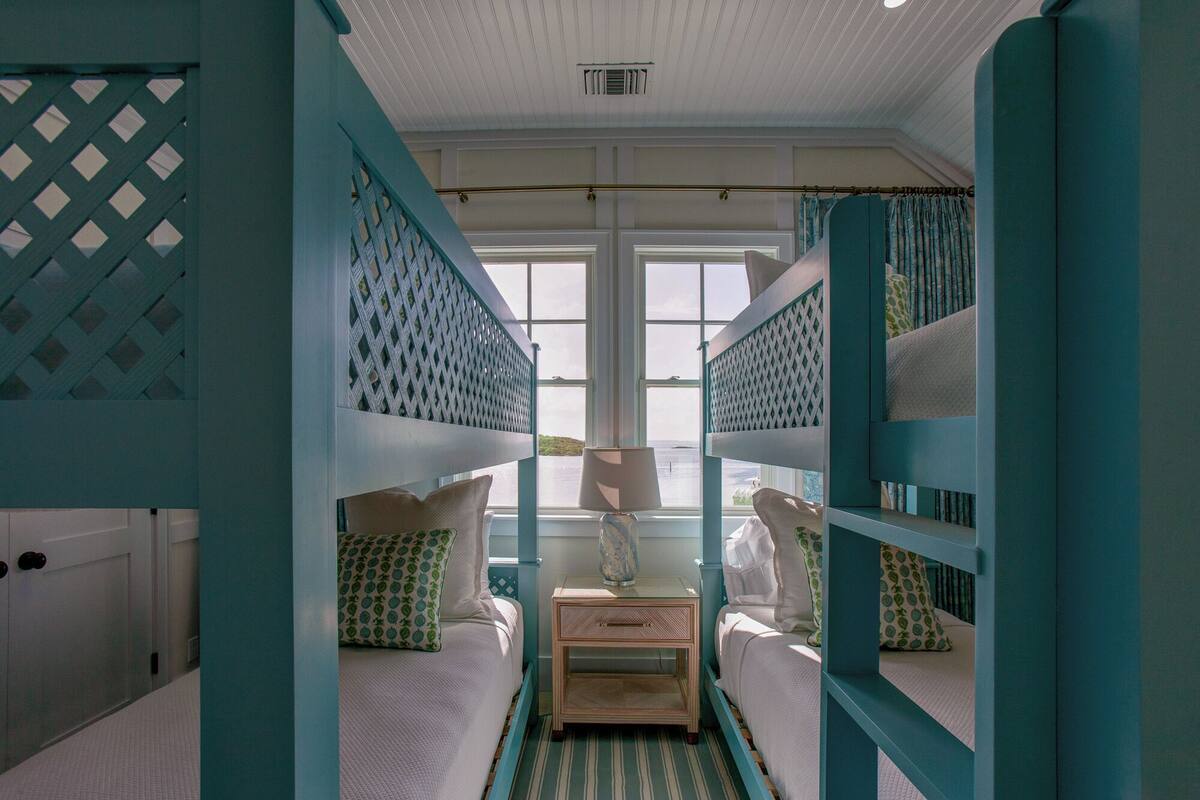 A room with bunk beds, a bedside table with a lamp, and a view of the sea through large windows.