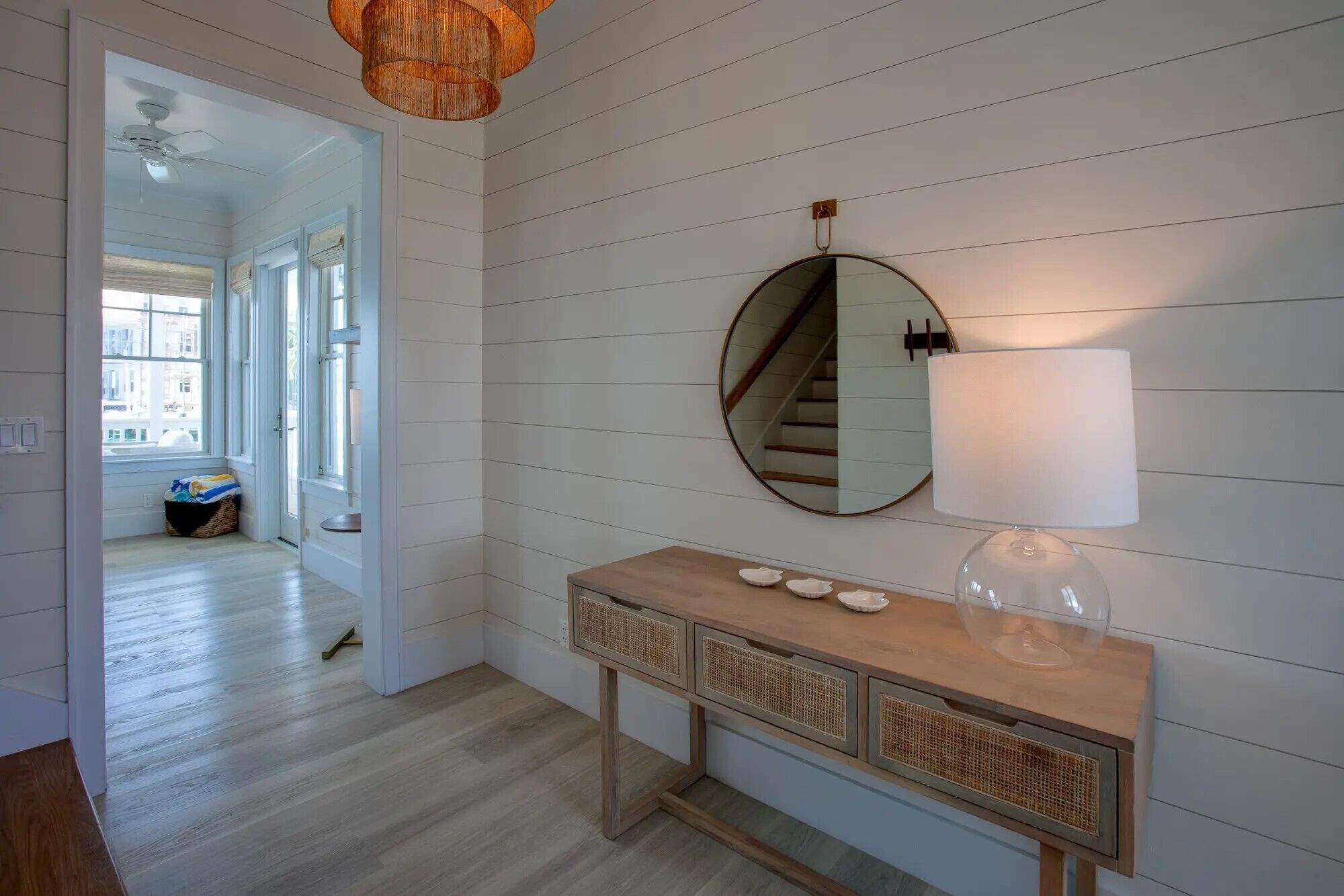 A hallway with a wooden console table, a round mirror, and a wall-mounted lamp.