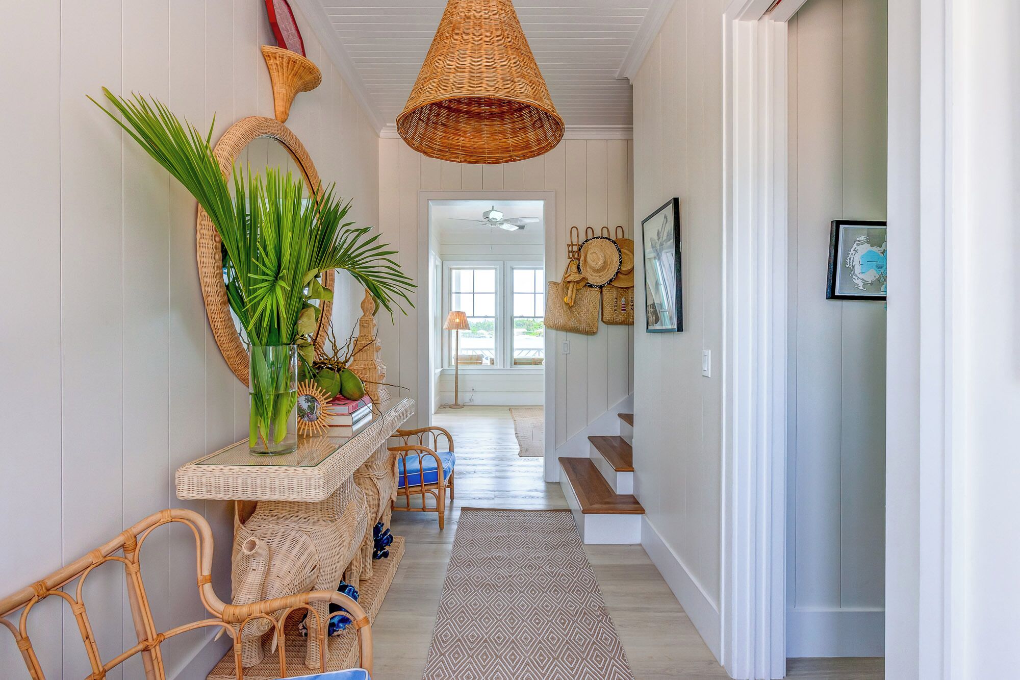 A hallway with wicker furniture, a hanging wicker lamp, and a patterned rug.