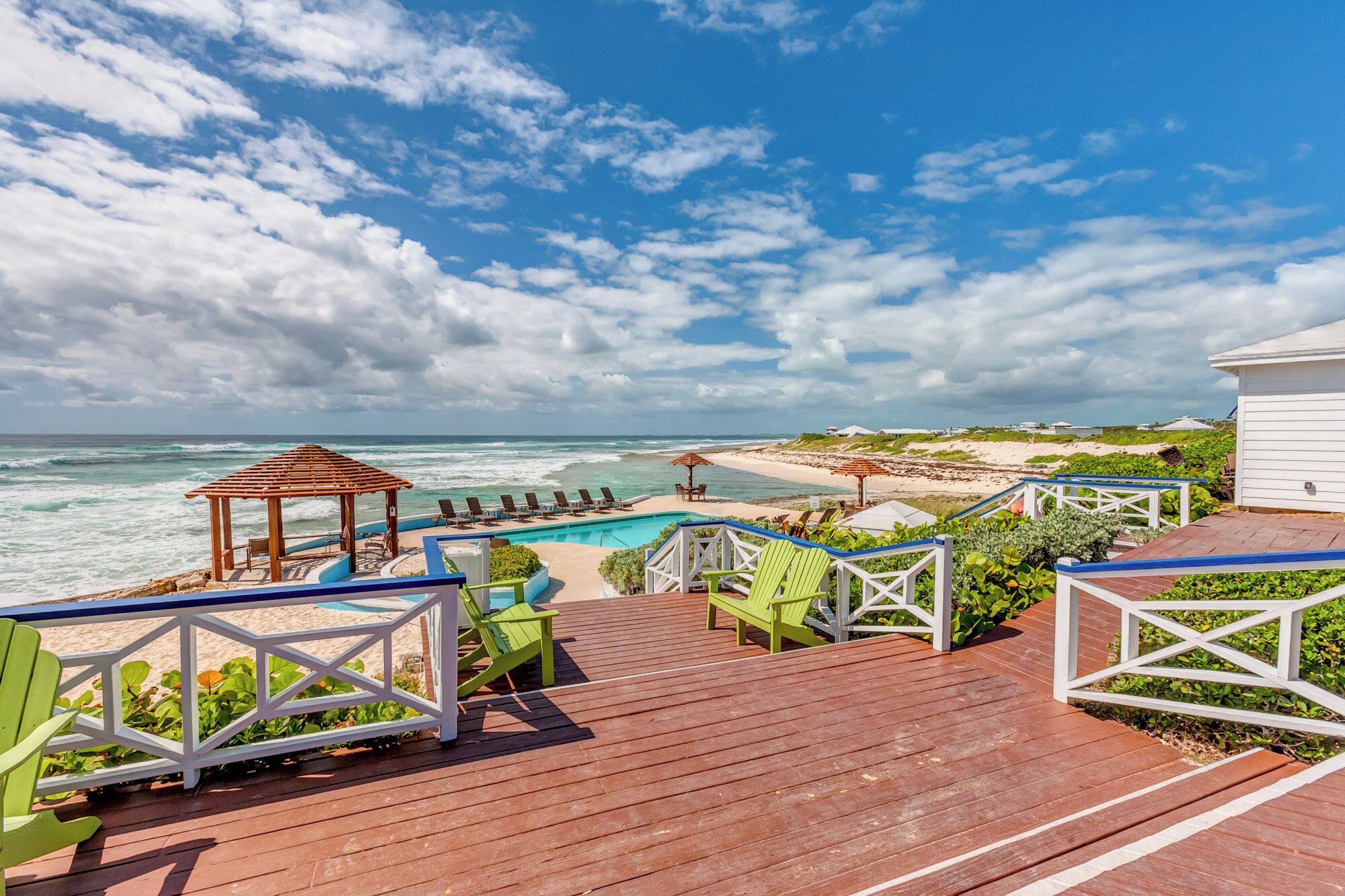 A wooden deck with a pool, beach chairs, and a gazebo overlooking the ocean.