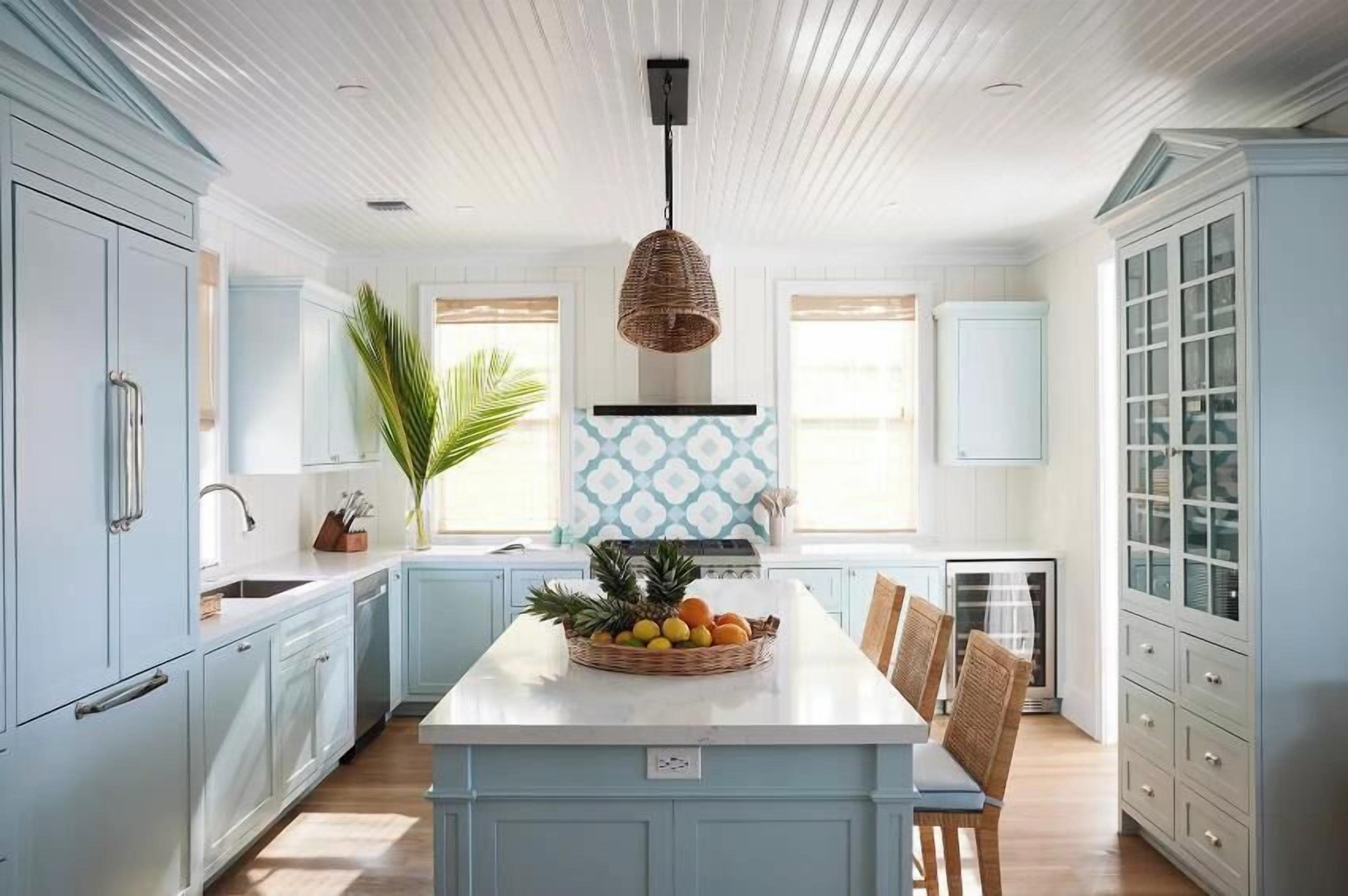 Una cocina con armarios azul claro, una isla central con fruta, un lámpara colgante y una ventana con vistas decorativas.