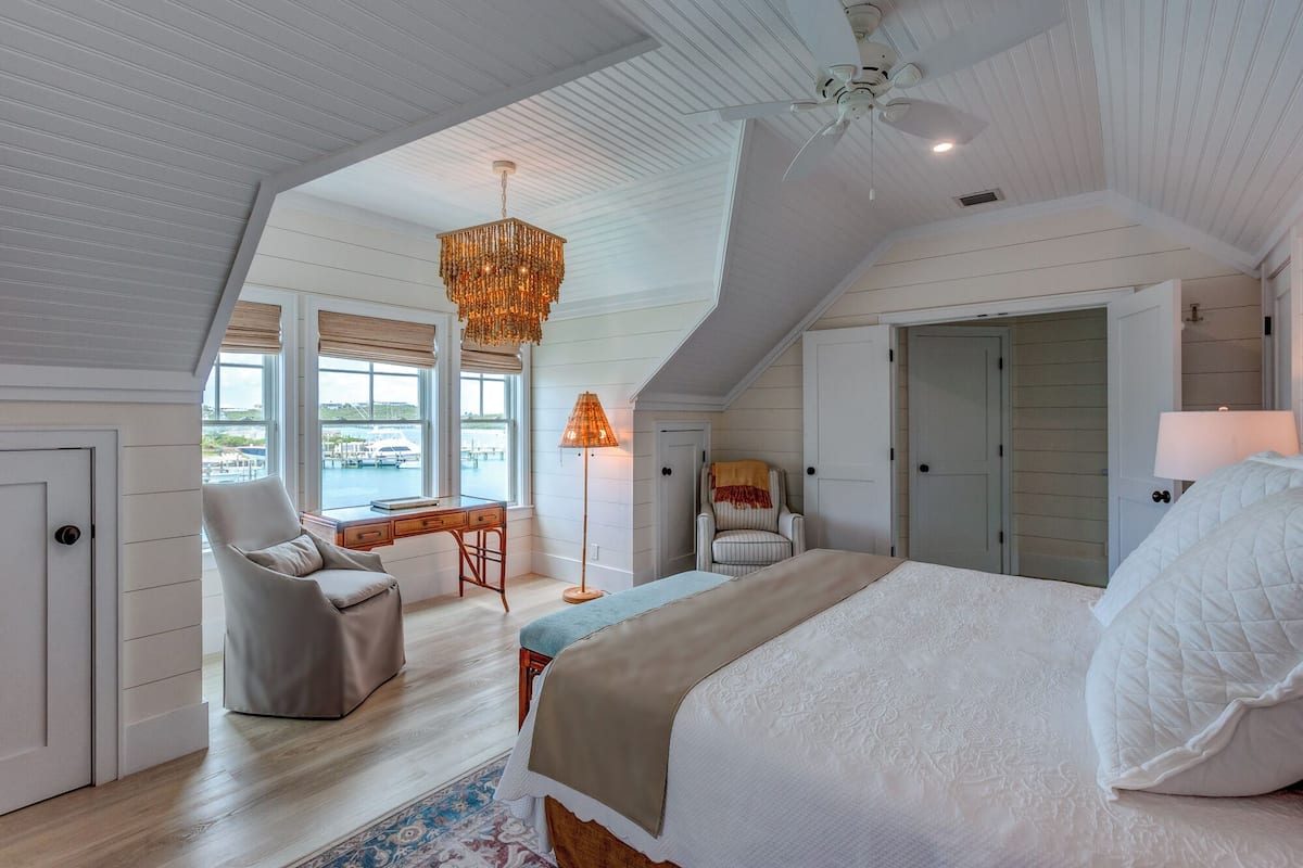 A bedroom with a large bed, a desk, a chair, and a view of the outside.