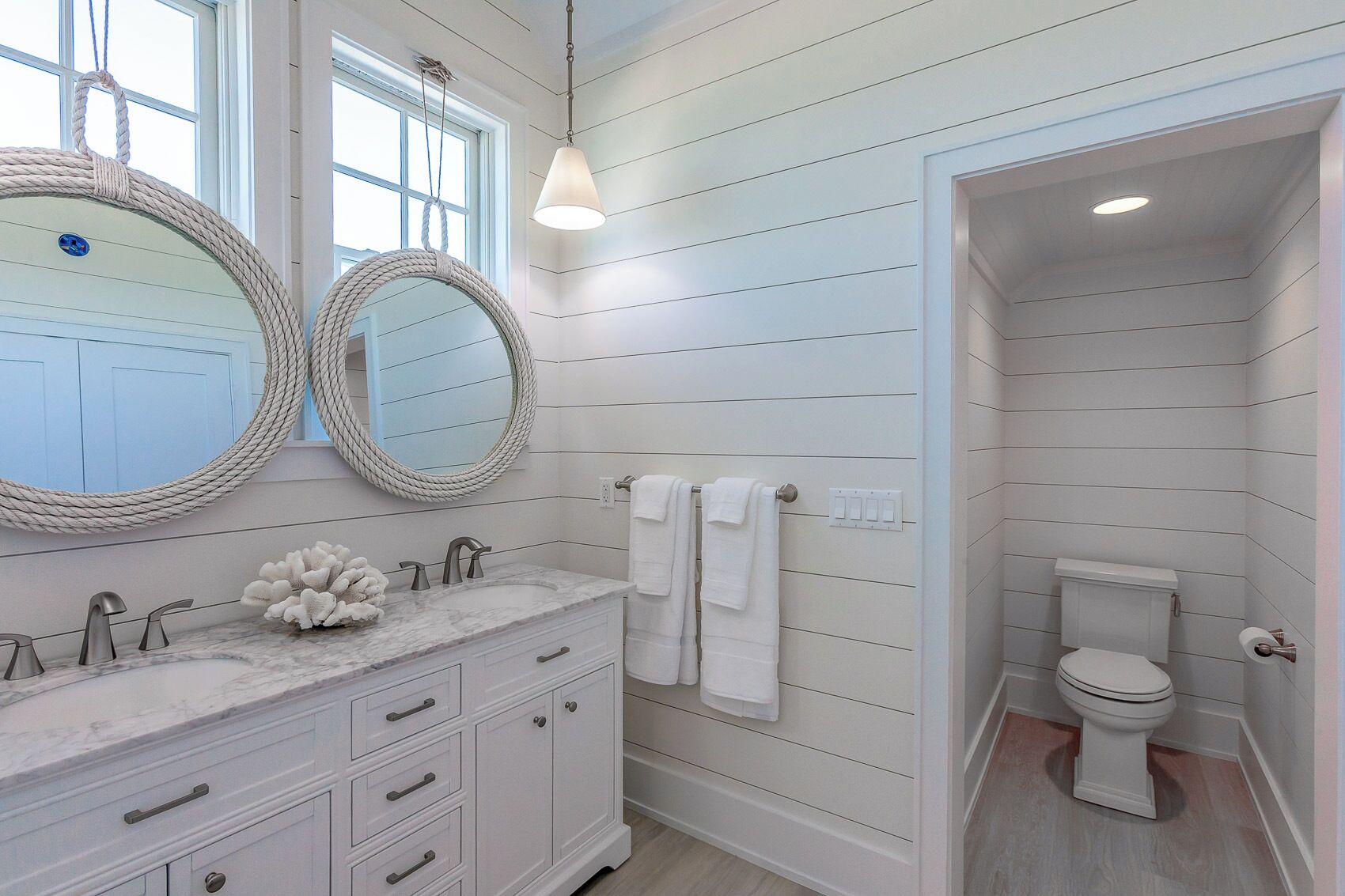 Une salle de bain avec un meuble-lavabo blanc, deux miroirs ronds, des toilettes blanches et un luminaire suspendu.