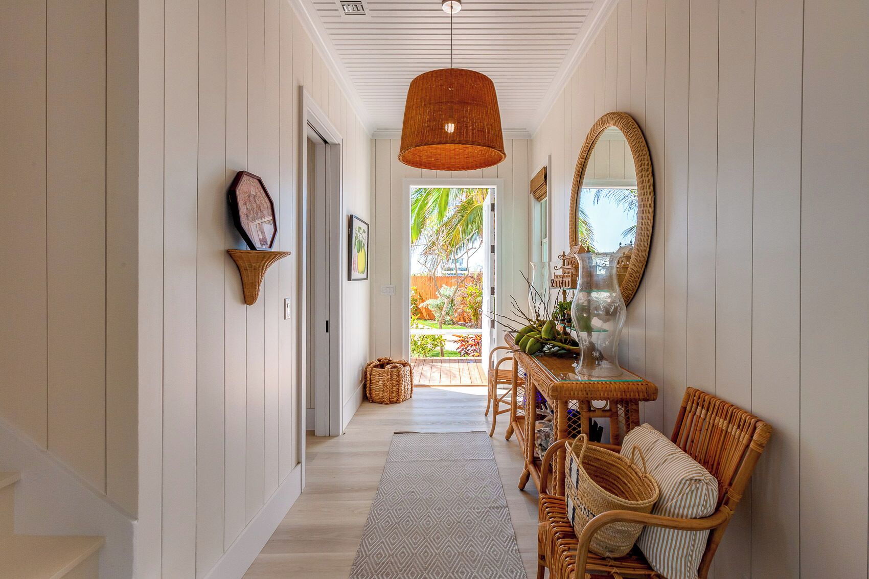A hallway with a dining area featuring wicker furniture and a large mirror.
