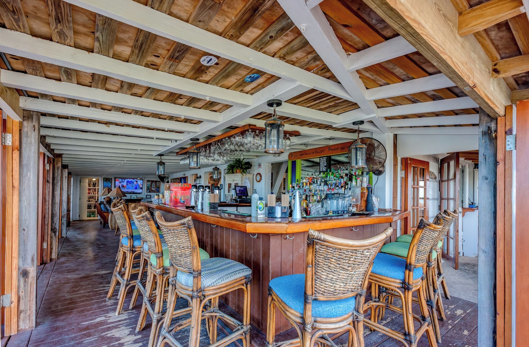 A bar area with wicker chairs, a counter with various bottles, and a television in the background.