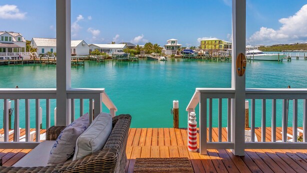 A wooden deck with wicker furniture and a view of a marina with boats and buildings. - The Abaco Inn (Hope Town)