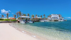 A beachfront property with clear water, a sandy beach, and several boats docked near the shore. - The Abaco Inn (Hope Town)