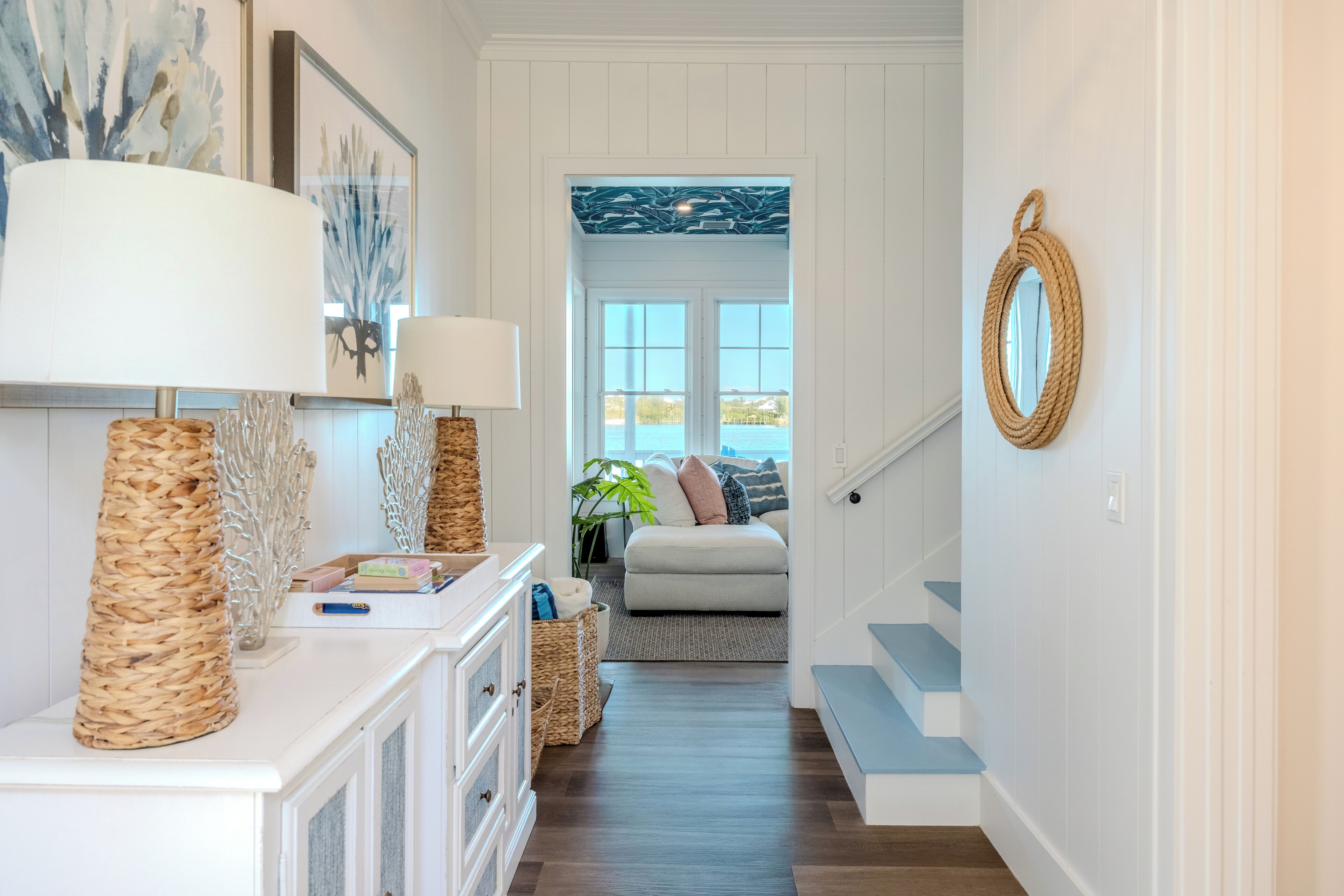 A hallway with a white dresser, wicker baskets, a lamp, and a mirror on the wall.