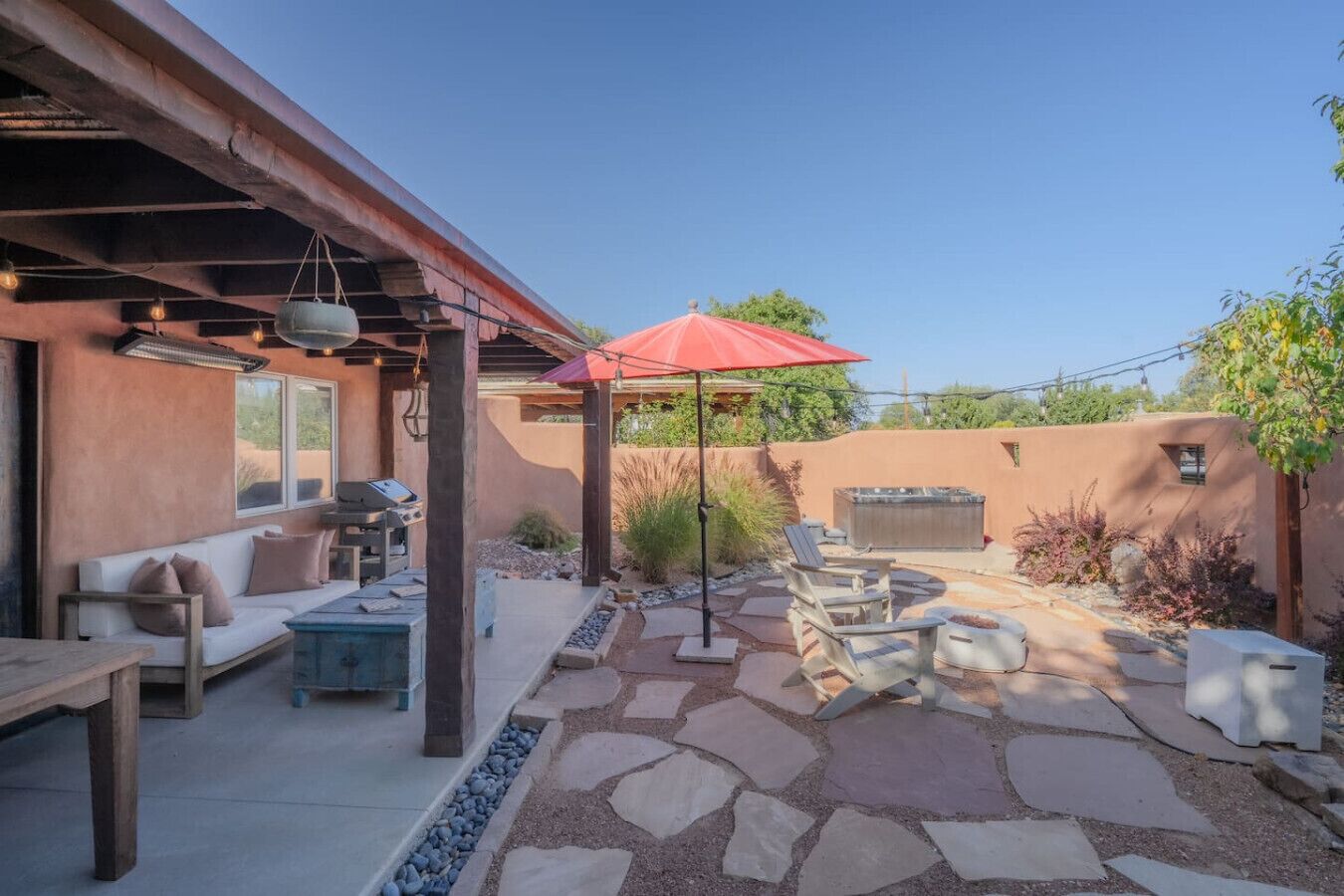 Une terrasse extérieure avec un sol en pierre, un barbecue, un canapé et un parasol rouge.
