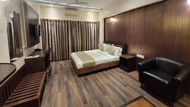 A modern hotel room with a wooden floor, a bed with a headboard, a desk with a chair, a leather armchair, and a TV mounted on the wall. - R D HOTELS HSR (Bengaluru)