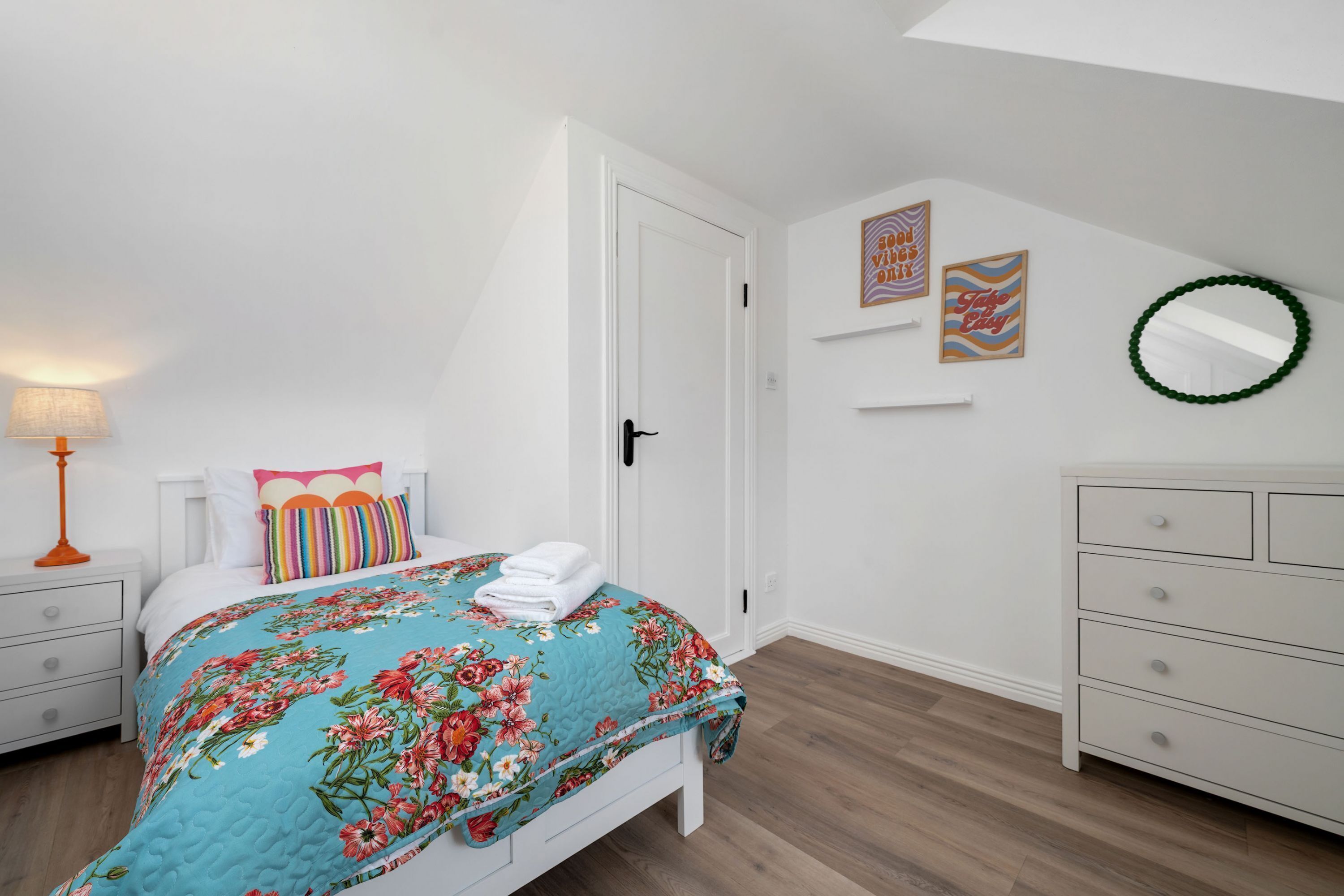 A bedroom with a bed, nightstands, a dresser, and a wall with framed pictures and a mirror.