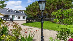 Ein gepflegter Garten mit Kiesweg, einer traditionellen Straßenlaterne und einem weißen Gebäude mit grauem Dach.