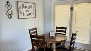 A dining area with a round wooden table, four chairs, a ceiling fan, and a window with blinds. - Cozy 3-Bedroom Ranch style house with Huge Backyard & Fire pit (Indianapolis)