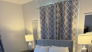 A neatly made bed with white bedding, two bedside tables with lamps, and a patterned curtain. - Cozy 3-Bedroom Ranch style house with Huge Backyard & Fire pit (Indianapolis)