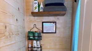 A compact bathroom with a toilet, a shelf with toiletries, a framed notice, and a broom.