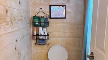 A compact bathroom with a toilet, a shelf with toiletries, a framed notice, and a broom.