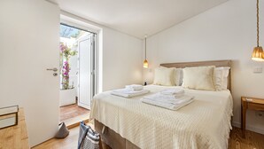 Une chambre avec un grand lit, une table de chevet, une lampe suspendue et une vue sur un jardin par une porte ouverte.