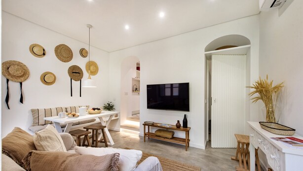 Un salon moderne avec un canapé, une table à manger, un téléviseur et des chapeaux décoratifs accrochés au mur.