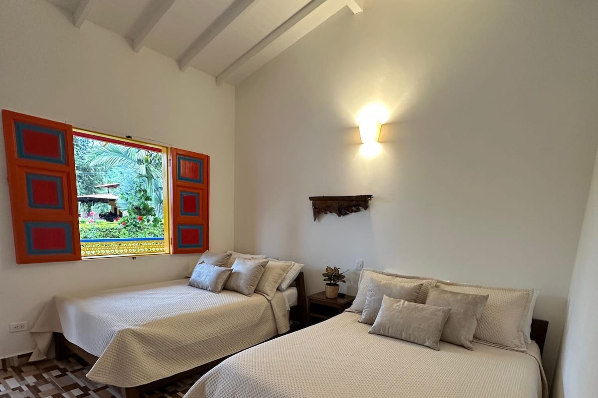 Una stanza con due letti, una finestra vista su spazi verdi, una lampada a parete e un pavimento decorato.