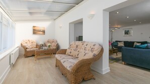 Un salón moderno con muebles de mimbre, un sofá azul y vistas al cuarto contiguo.