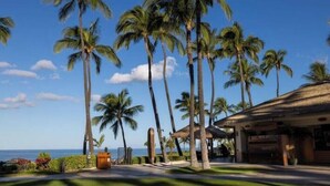 A resort with palm trees, a thatched-roof building, and a view of the ocean. - View Stunning Sunsets in this Ocean View 1 Br @ MVC Ko Olina Beach Club (Kapolei)