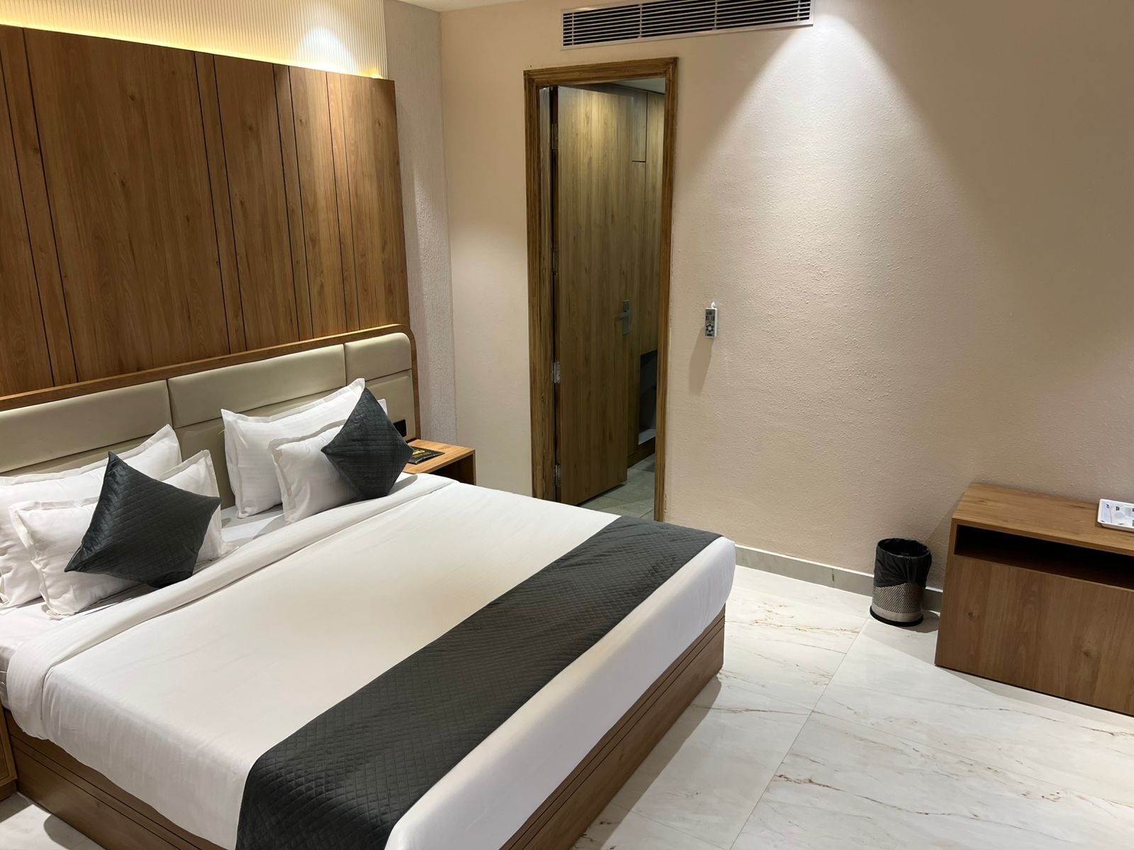 Una cama bien hecha con ropa de cama blanca y negra, un cabecero de madera y una mesita de noche con un libro.