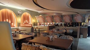 Un restaurante moderno con mesas redondas y sillas con estampado floral, una zona de bar y un área de estar con bancos acolchados.